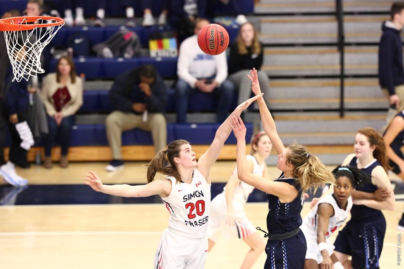SFU player reaching up with their hand to block an opponent's shot from going in.