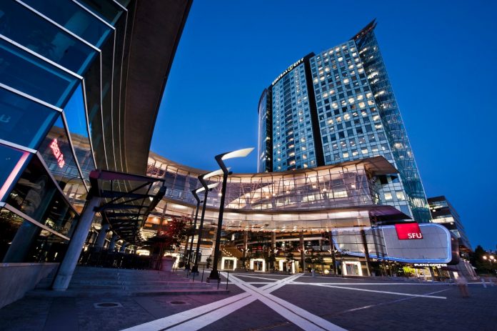 A photo of the outside of SFU Surrey campus’ entryway atrium. The image looks slightly stretched out, but is otherwise pretty recognizable. The photo was taken at dusk, accenting the building’s lighting.