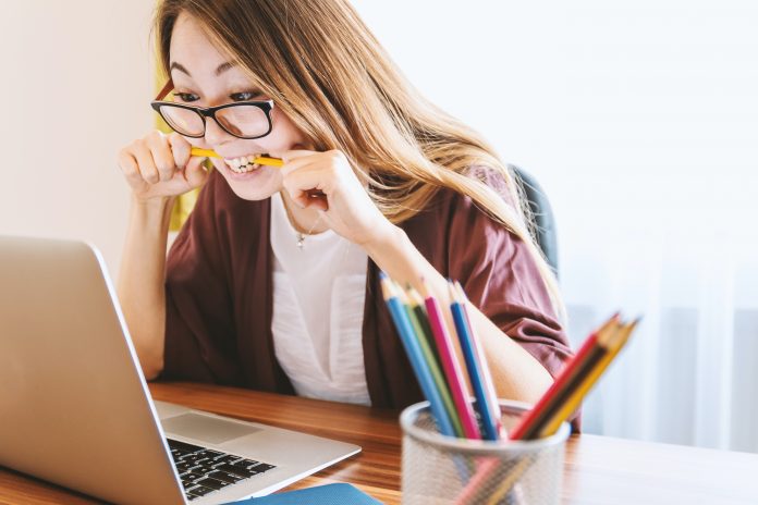 Woman holds and bites pencil staring at laptop screen.