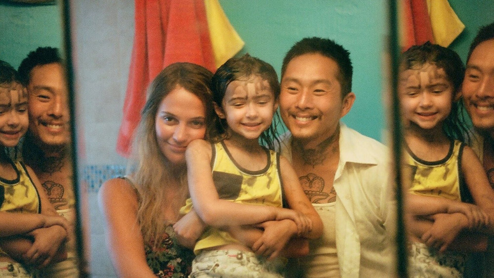 A mixed race couple with their young daughter. The family stare into a mirror, smiling.