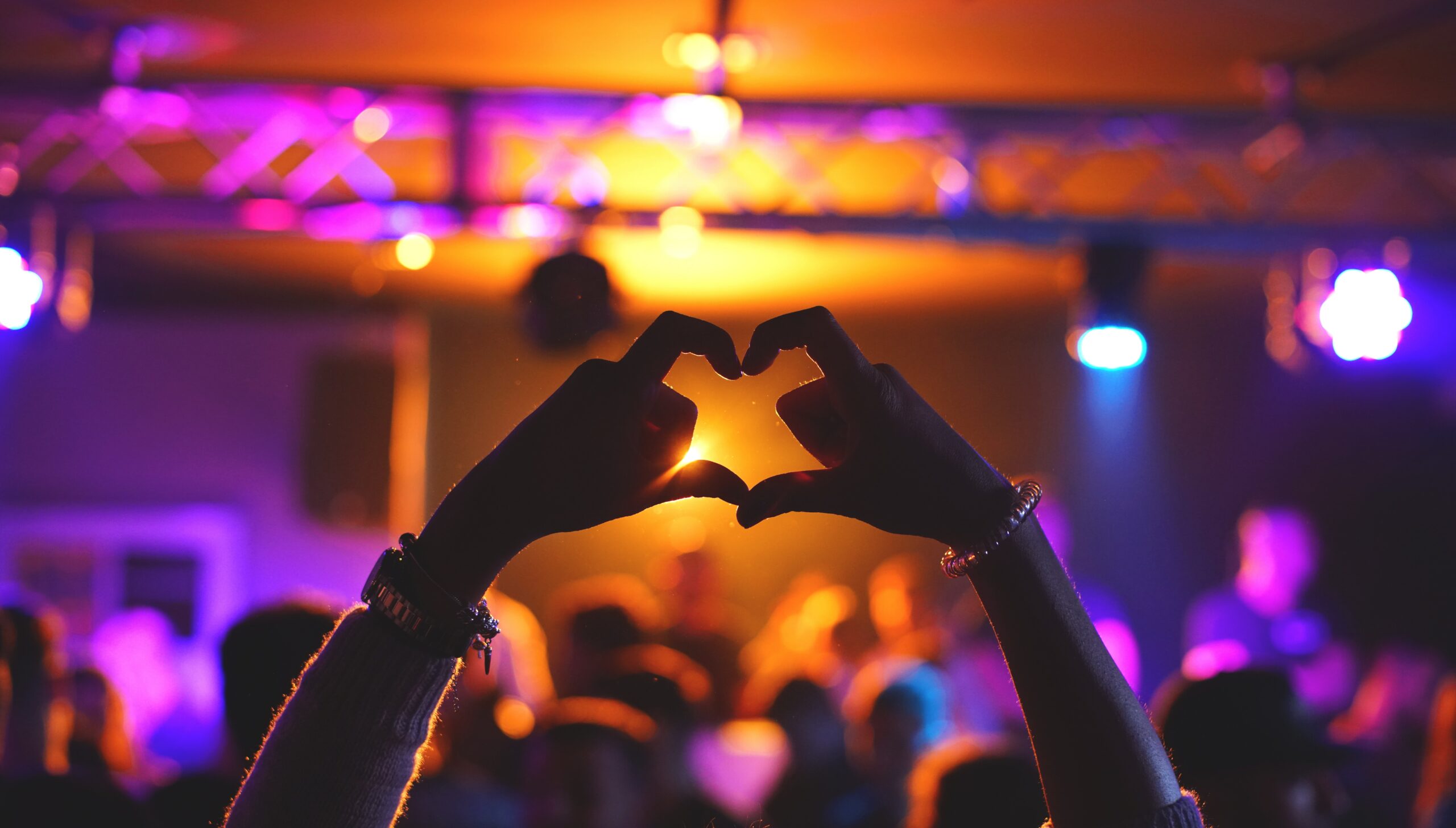fingers in heart shape above a busy club with pink and yellow lighting