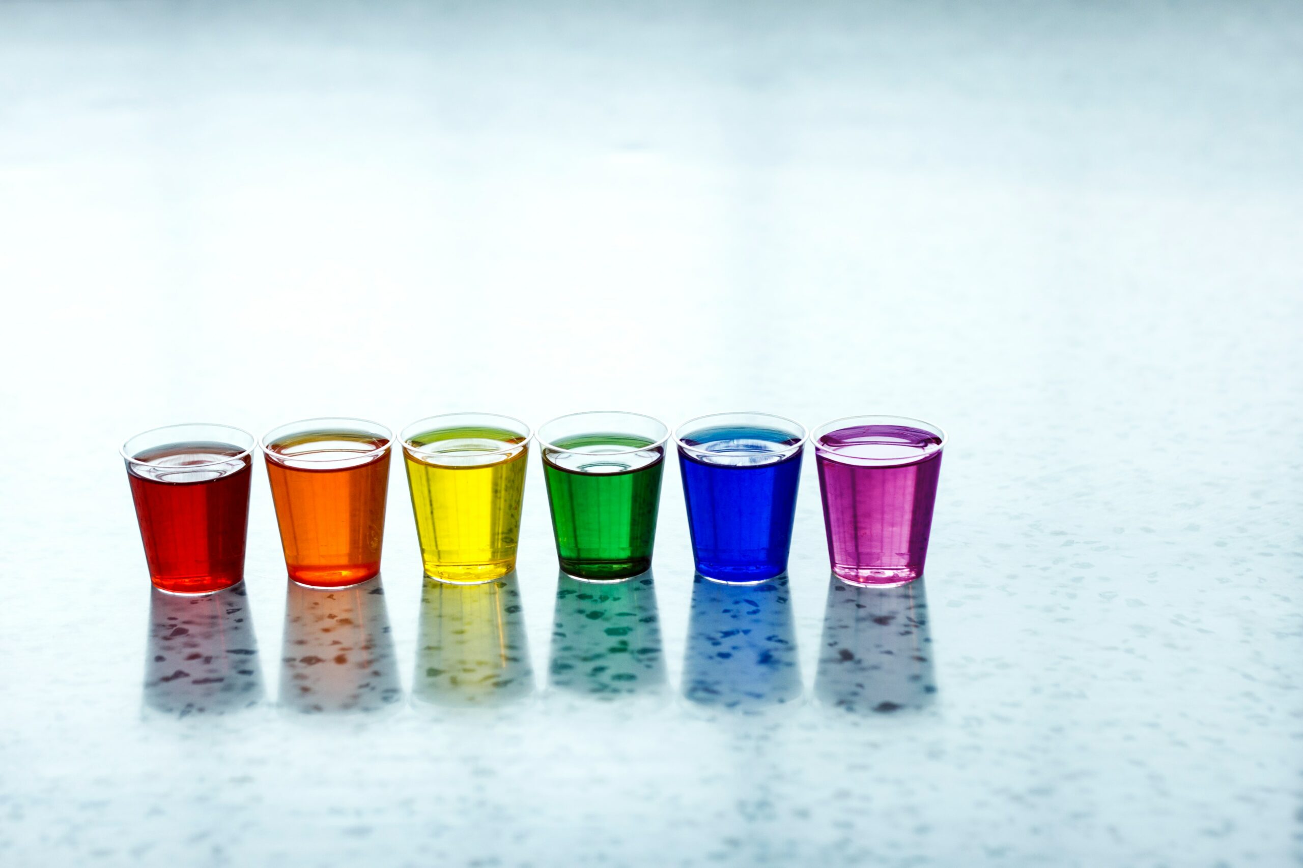 six full shot glasses. they have red, orange, yellow, green, blue, and violet liquids