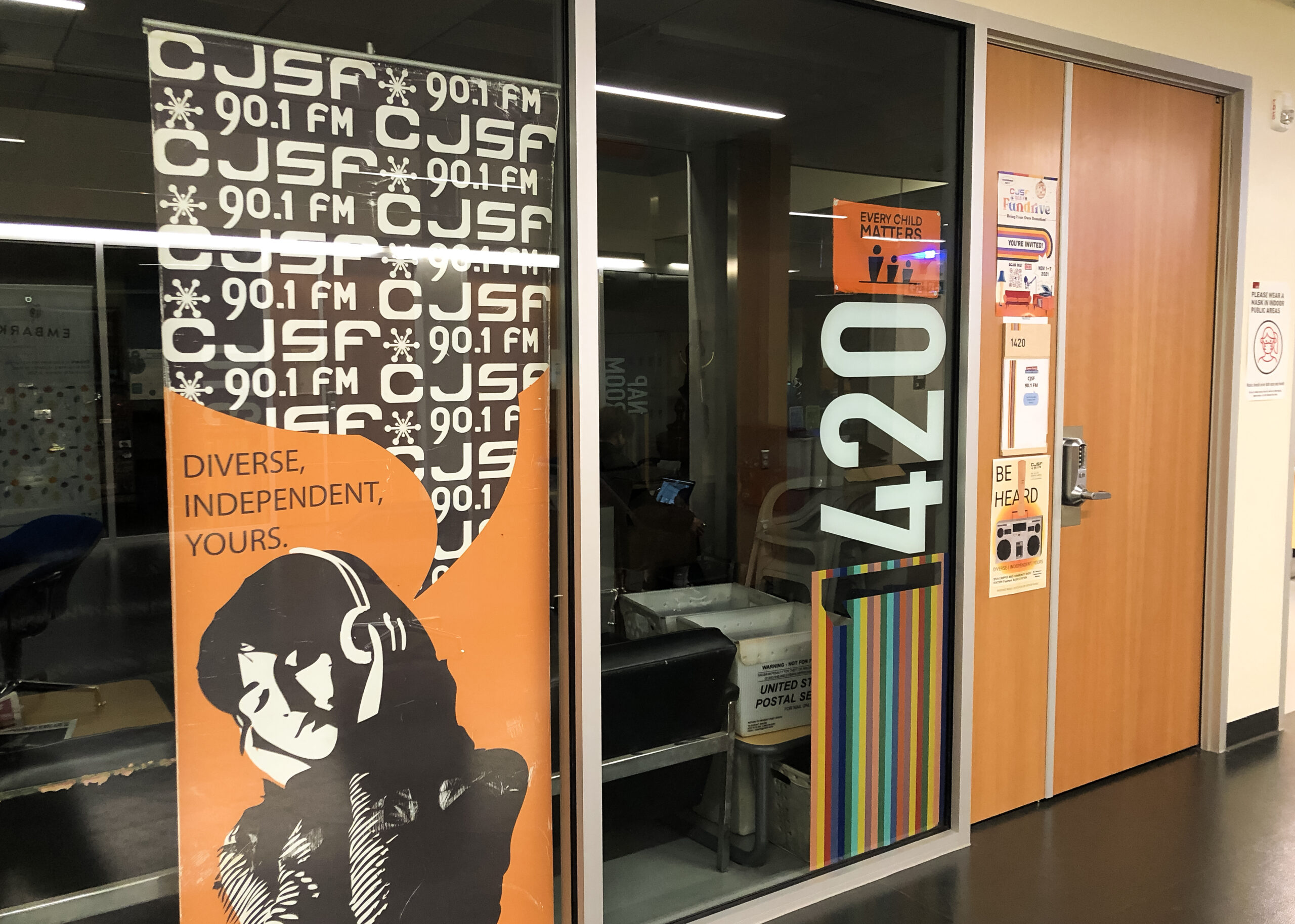 Exterior of the CJSF radio station. An orange banner with their slogan “Diverse, Independent, Yours” can be seen from the floor to ceiling windows
