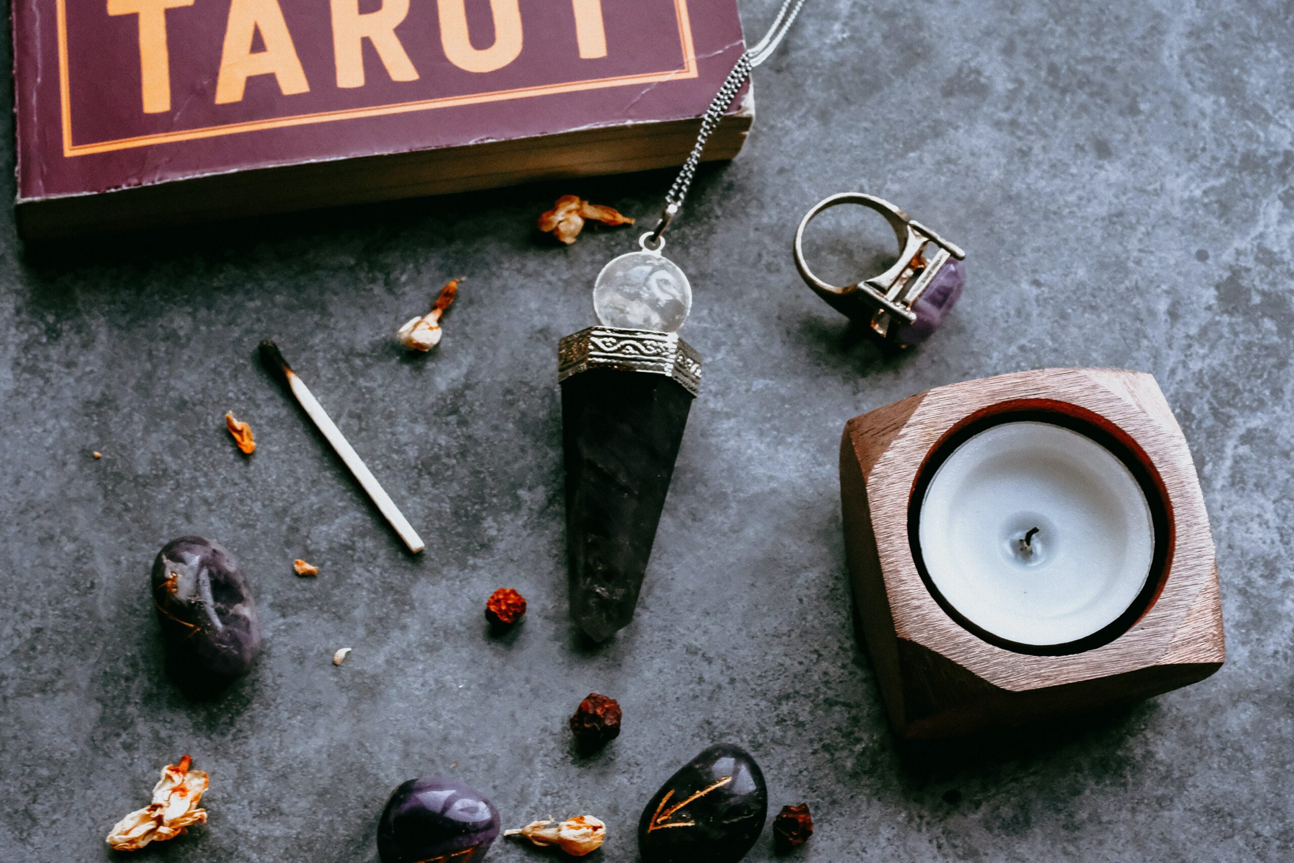 A candle, tarot book, and black and purple stone jewelry laid on a table