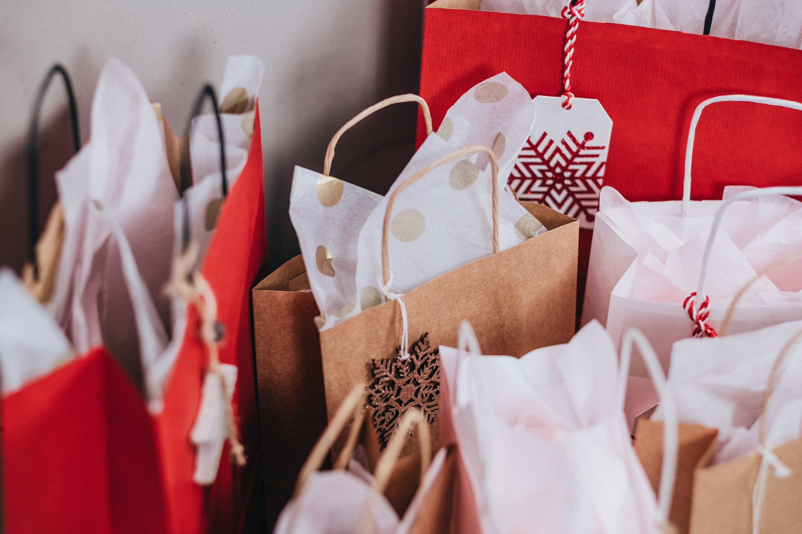 A bunch of gift bags in red and brown, with white and gold tissue paper peeking out from each. The bags also feature glittery snowflake tags, tied with red and white string