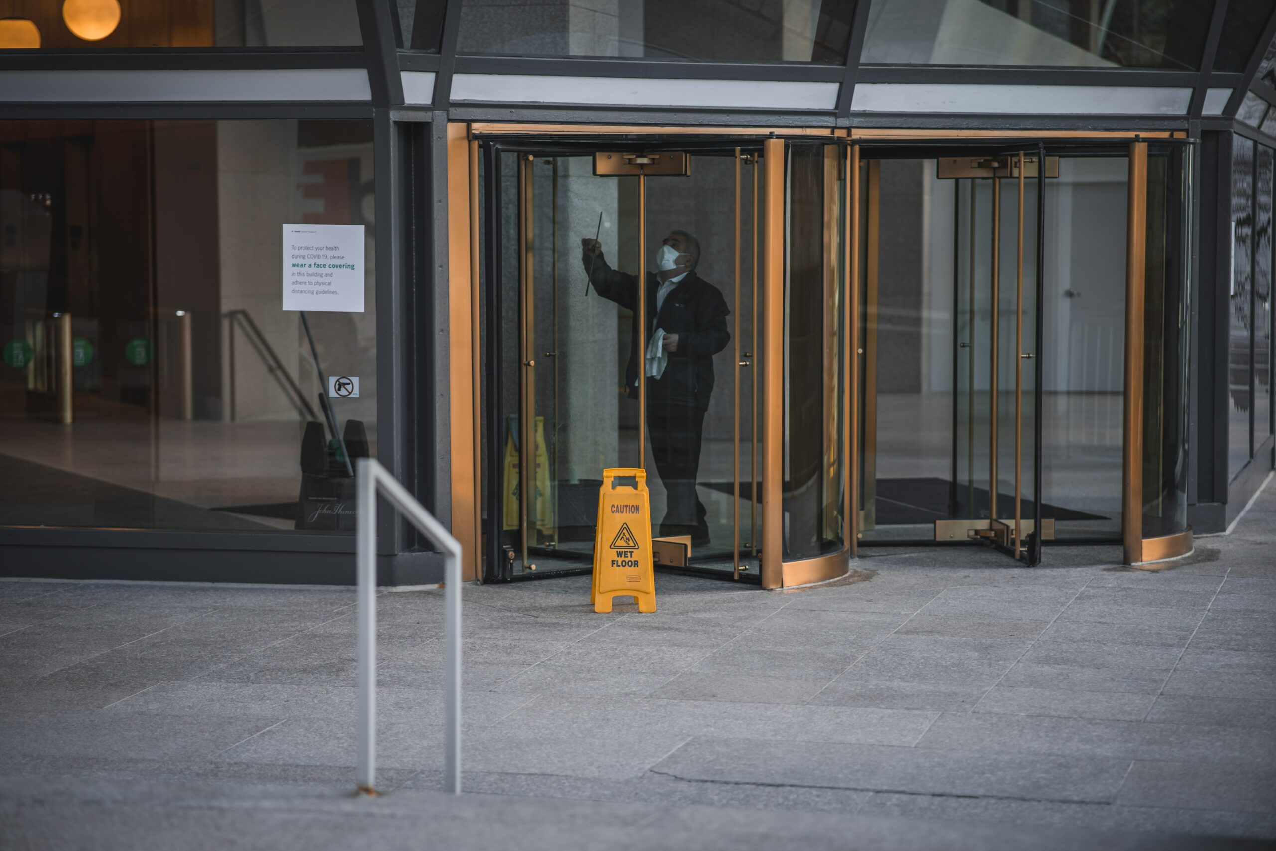 faraway shot of a cleaning worker wiping a revolving door with a yellow slip warning sign