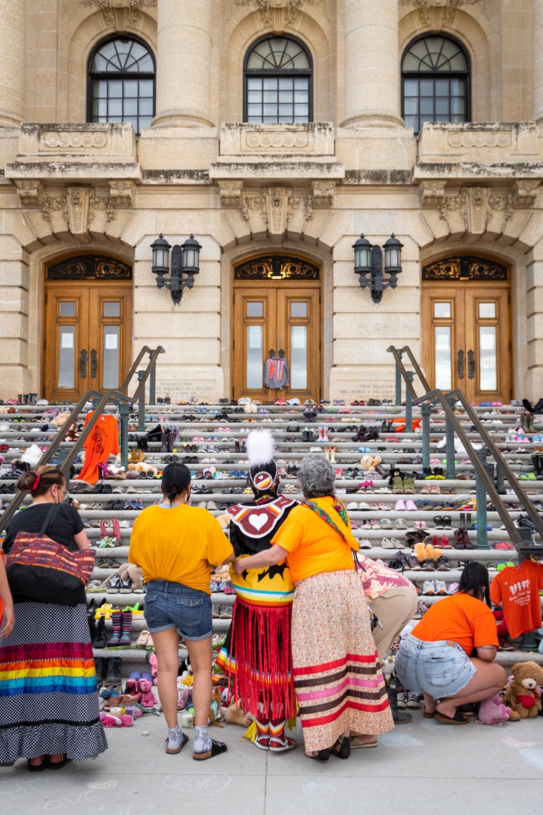 three people, one in Indigenous garment, looking at a staircase full of toys