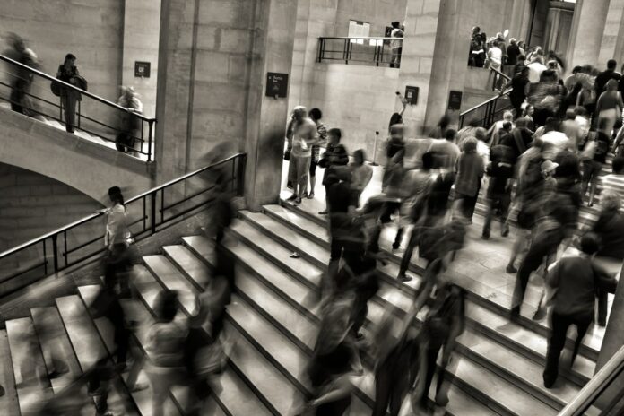 Image courtesy of José Martín Ramírez Carrasco / Unsplash A black and white photo of many people walking up and down stairs. The photo is blurred lightly, giving the impression of movement.