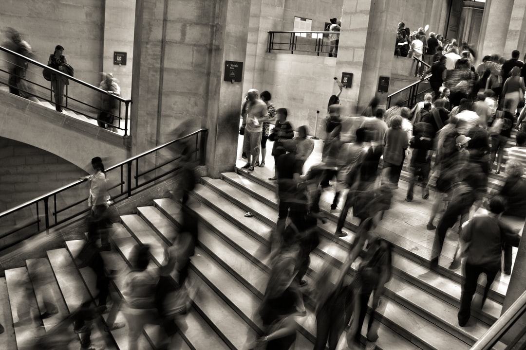 A black and white photo of many people walking up and down stairs. The photo is blurred lightly, giving the impression of movement.