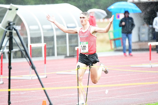 A photo of SFU cross country runner Aaron Ahl with his hands outreached above his head as he approaches the finish line in the pouring rain.