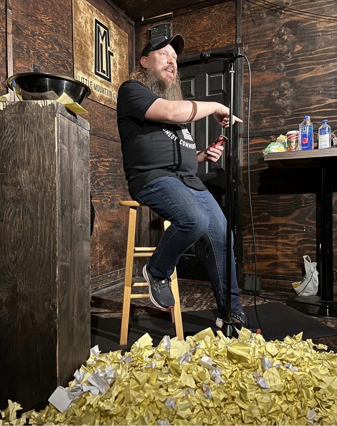 In a dark wood-panelled room, comedian Graham Clark (wearing a Little Mountain Gallery shirt and sporting an impressively long beard) addresses an unseen audience. A large pile of crumpled white and yellow notepapers is at his feet.