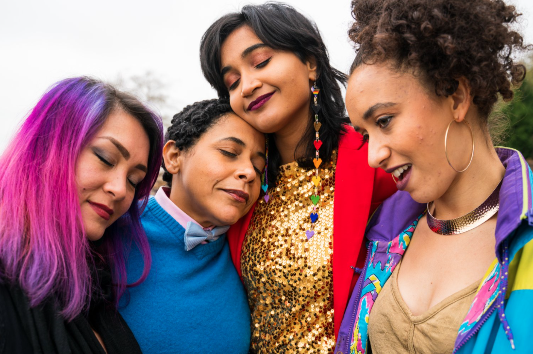 Four people huddled together, leaning into one another with content expressions on their faces. All except the one on the far right have their eyes closed.