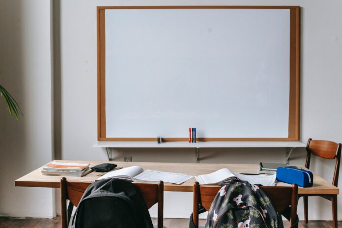 It's important to take breaks from academia School supplies and backpacks lie strewn about on a desk. A whiteboard is in the centre of the photo, and it is blank. Notebooks are open, but it looks like the students have walked off to do other things.