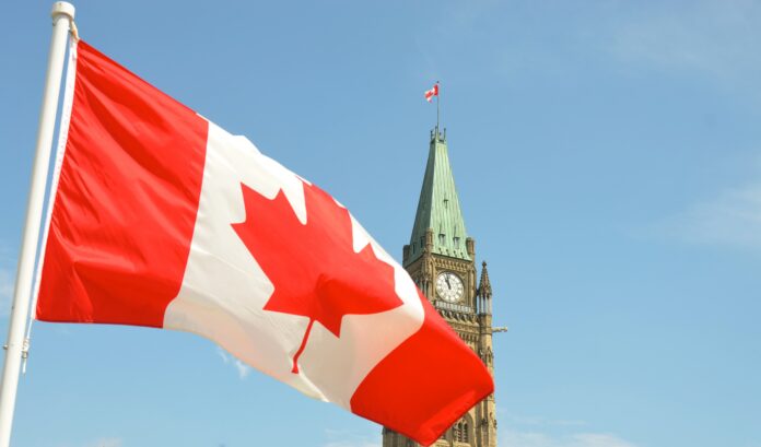Nice Canadian Stereotype The Canadian flag waves in front of a clear blue sky. The top of a Canadian Parliament building spears the sky in the background.