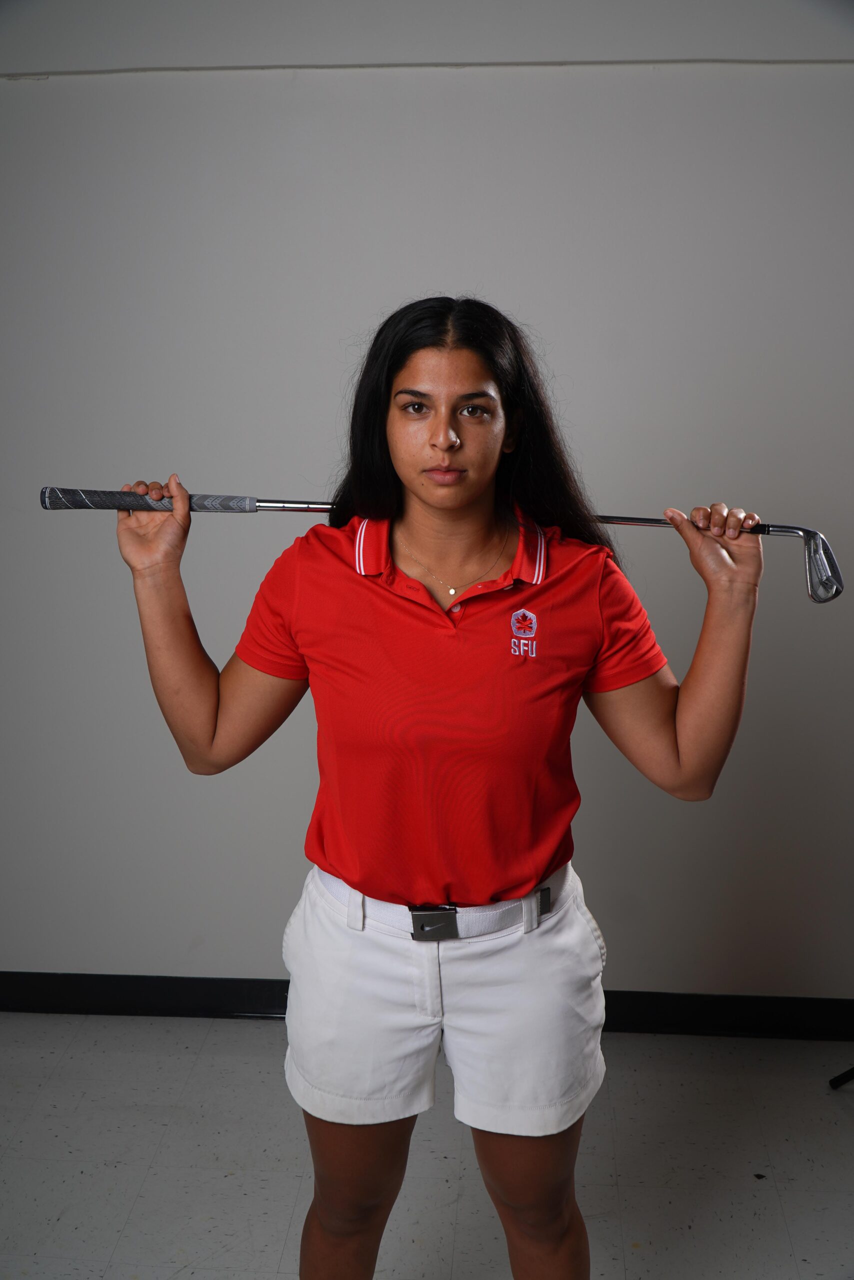 A photo of SFU golfer Shirin Anjarwalla posing for the camera in her SFU polo with a golf club behind her back.