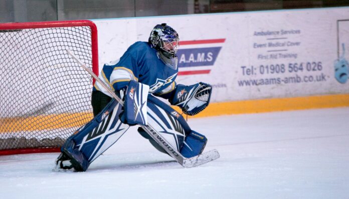 andy-hall-UqT1DUuZ6Yk-unsplash A shot of a goalie at the top of his crease with blue equipment, ready to face a shot.
