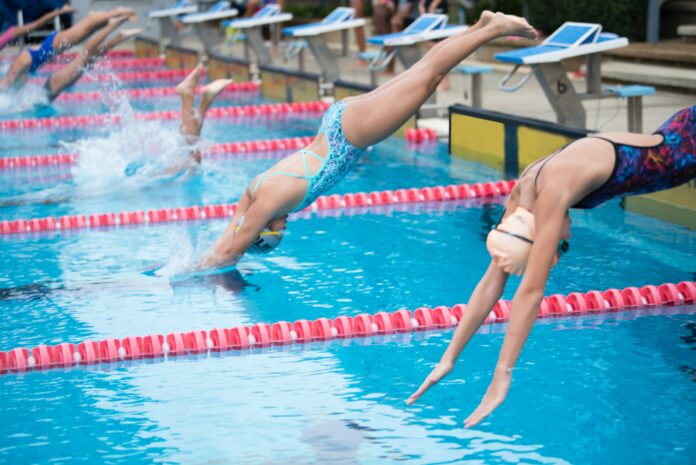 arisa-chattasa-AZcNLJgO4XE-unsplash (2) Photo of swimmers diving into the pool for their blocks.