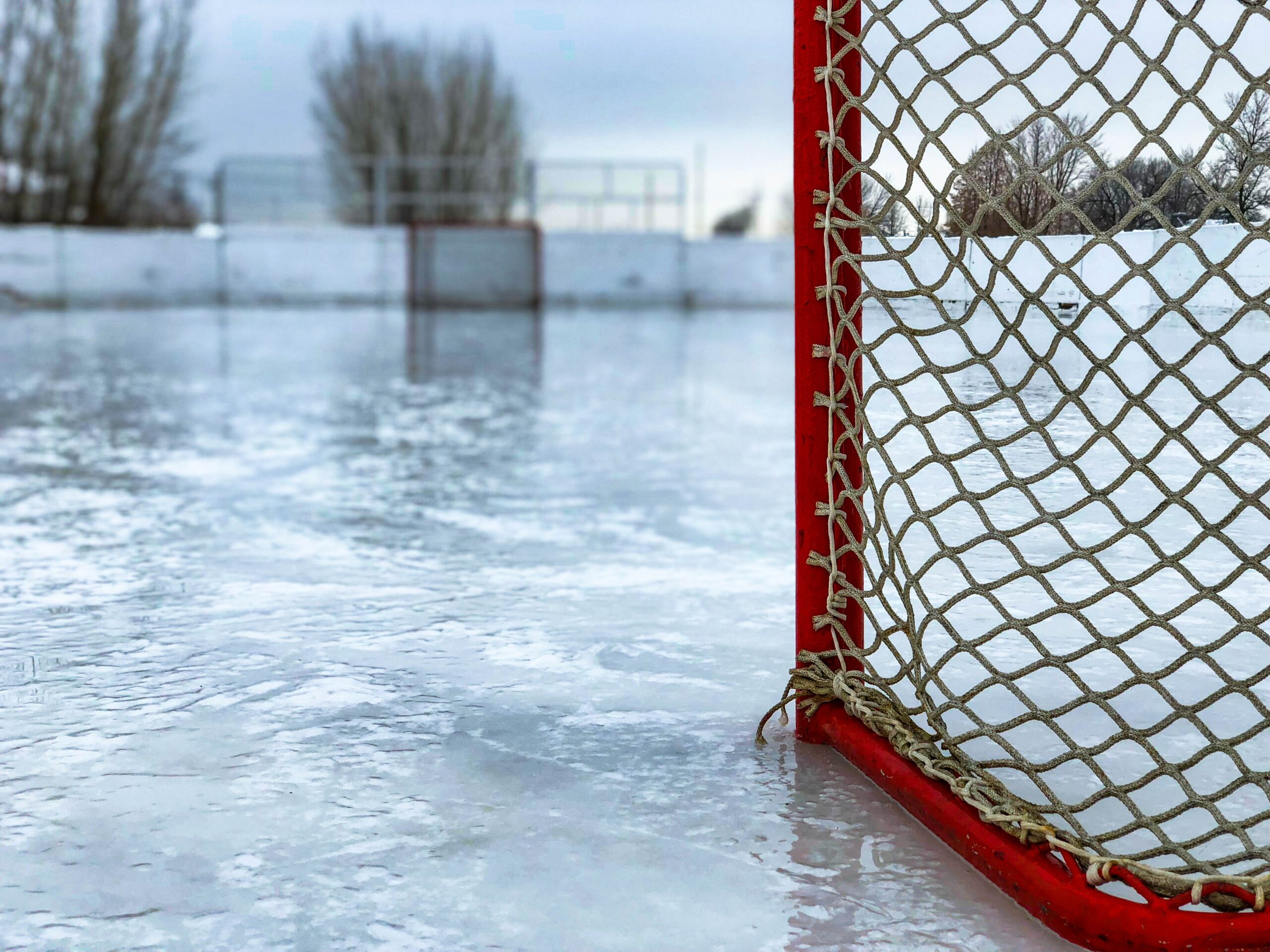 A close up shot of the back of a net on an outdoor hockey rink.