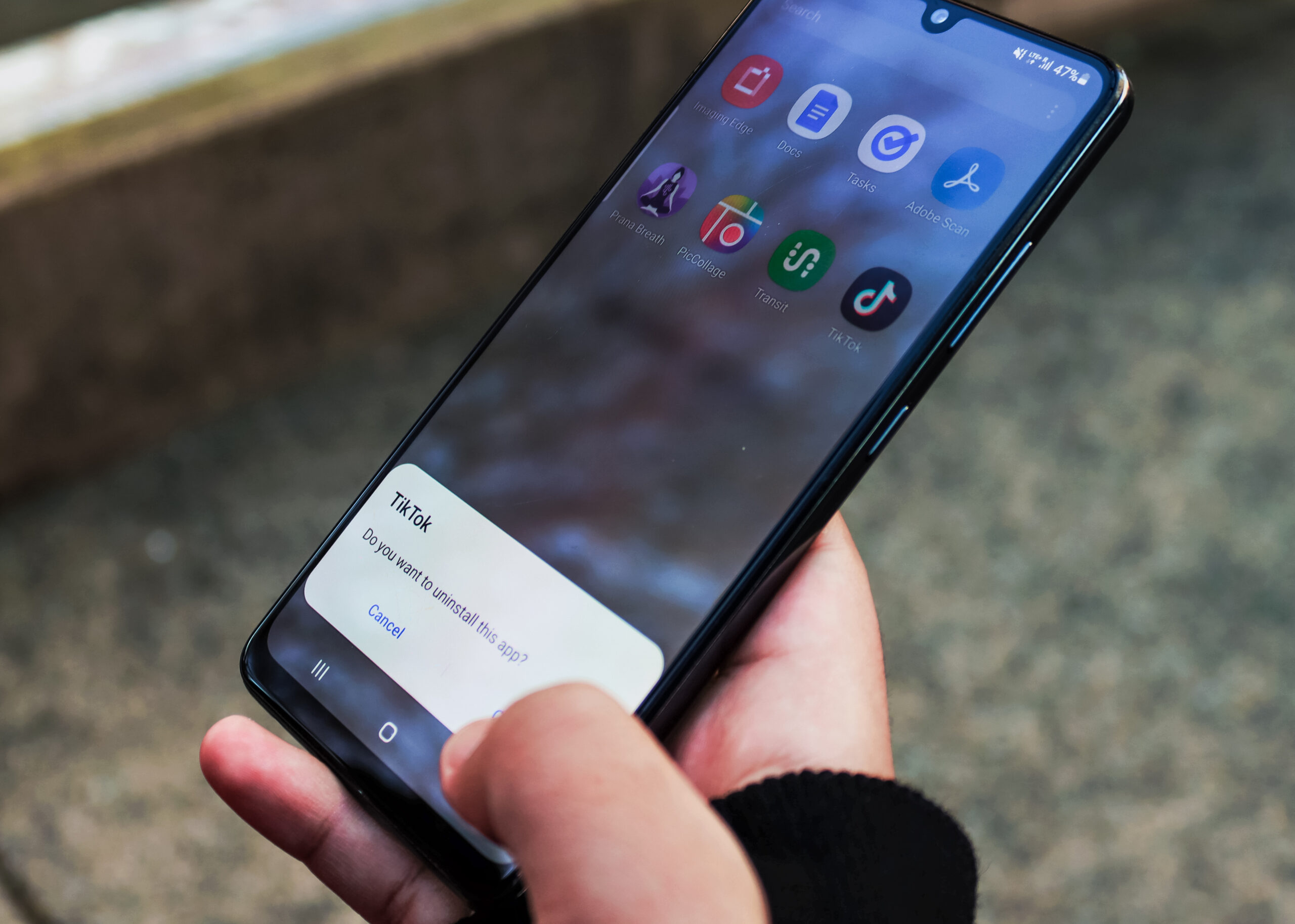 A photo shows someone holding a mobile phone. On the screen, a TikTok notification bar is asking: “Do you want to uninstall this app?” The person’s thumb hovers over they “Okay” button.