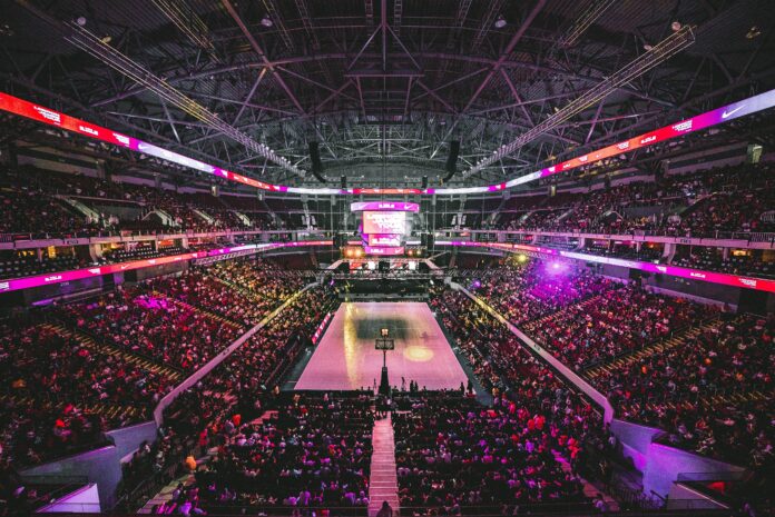 jc-gellidon-XmYSlYrupL8-unsplash (2) Stadium view of a basketball game packed with fans with the lights dimmed down.