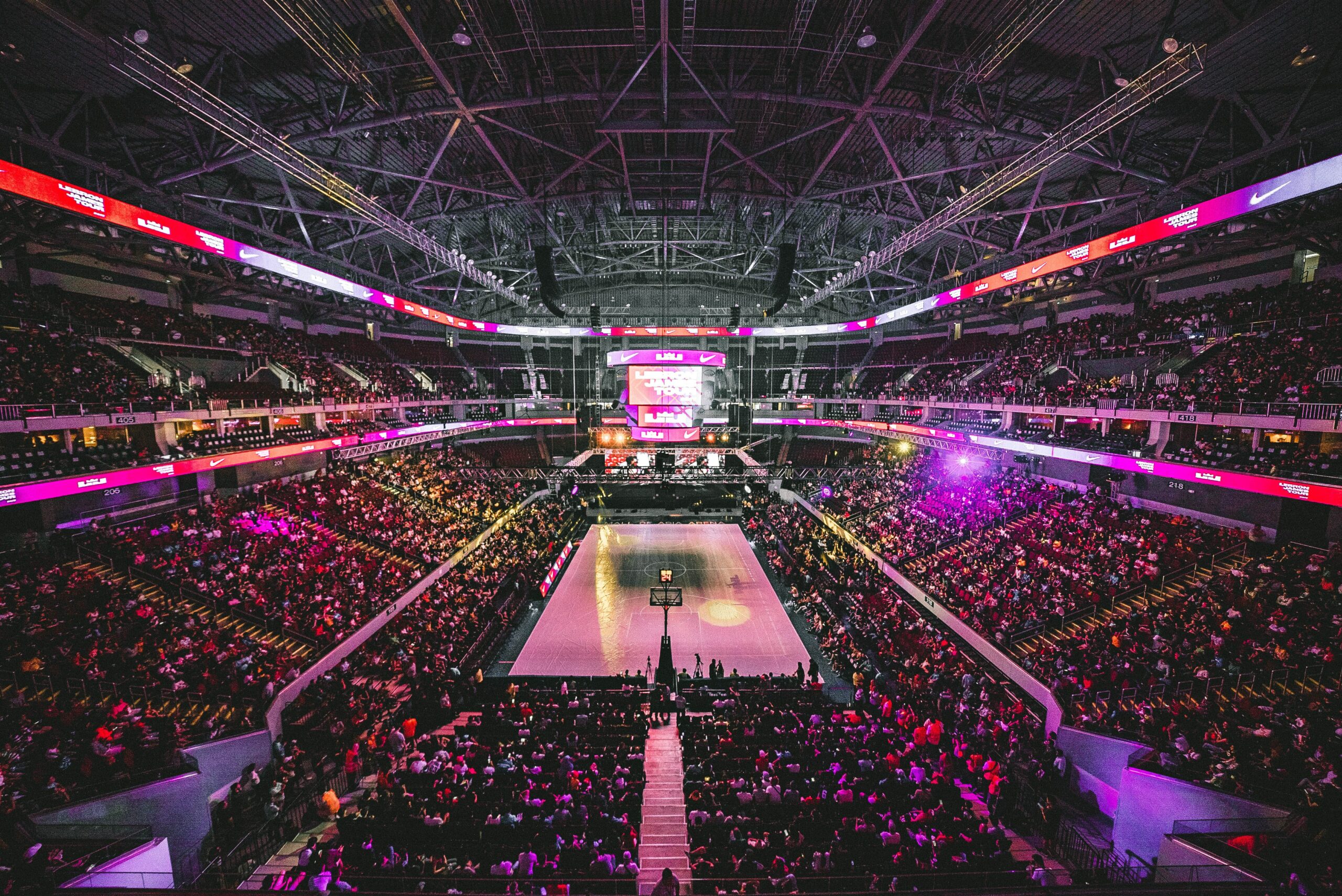 Stadium view of a basketball game packed with fans with the lights dimmed down.