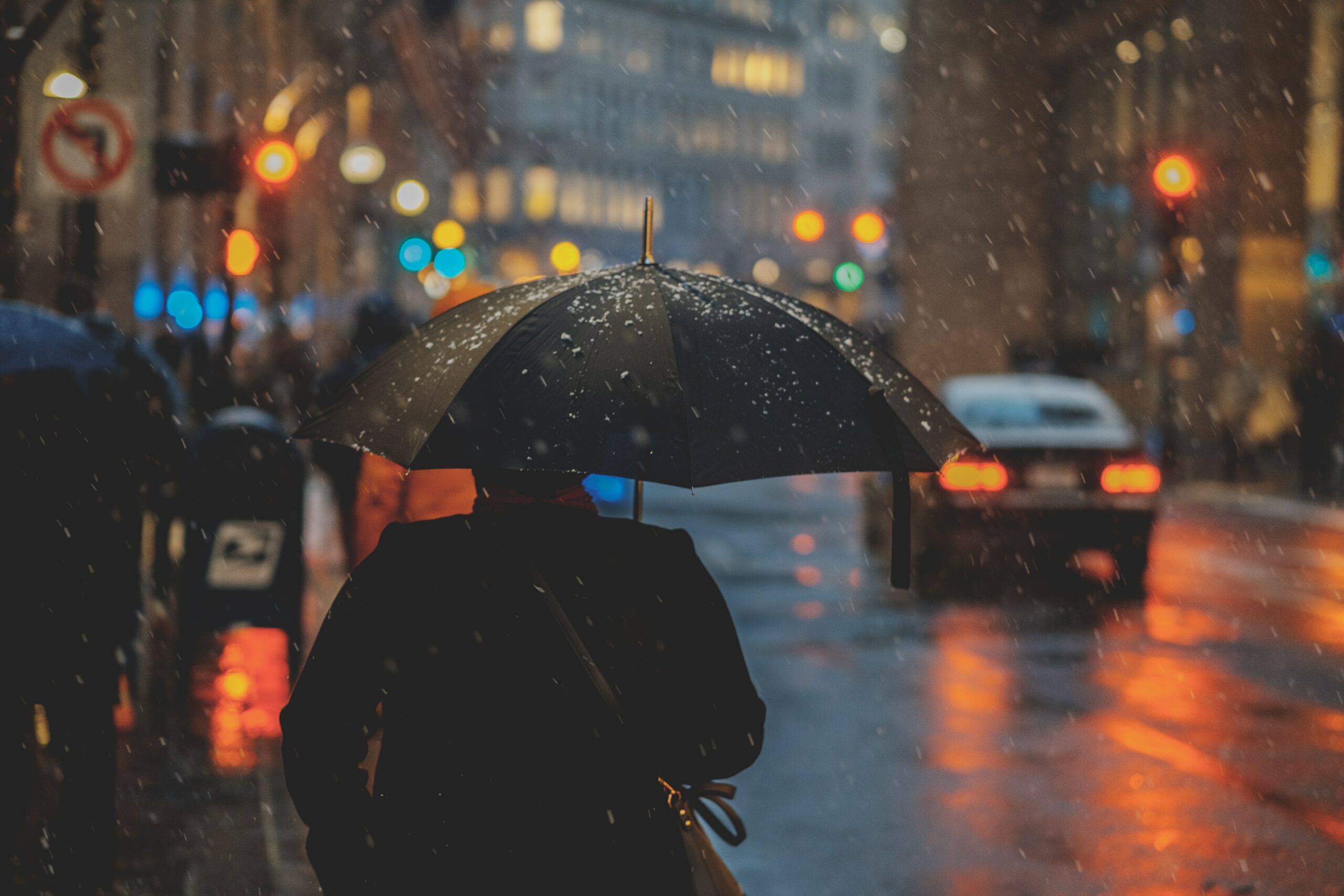 A person walking with an umbrella in the pouring rain downtown.