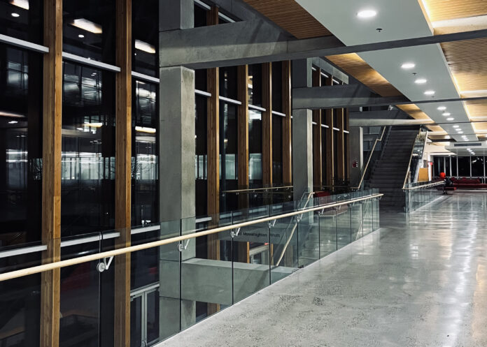 A very empty hallway with windows all along the left side facing a dark night sky.