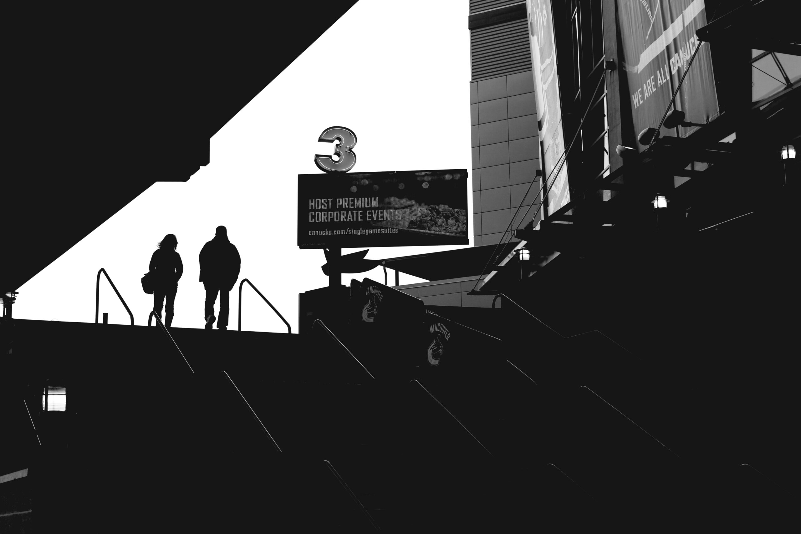 Black and white photo of two people heading into Rogers Arena at a side entrance