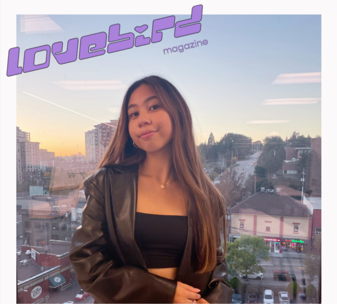 web cover-3 Portrait of Jaymee, a woman with long brown hair wearing a black crop top and leather jacket. Above, in stylized purple letters, text reads “Lovebird Magazine.”