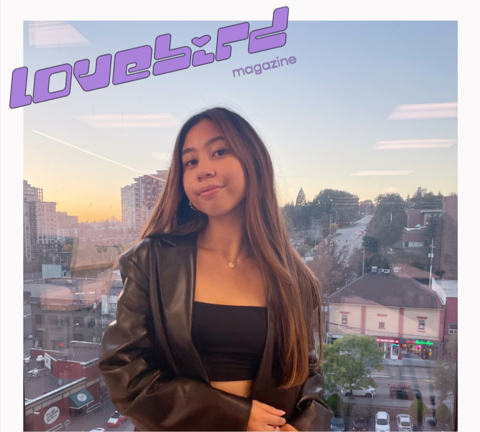 Portrait of Jaymee, a woman with long brown hair wearing a black crop top and leather jacket. Above, in stylized purple letters, text reads “Lovebird Magazine.”