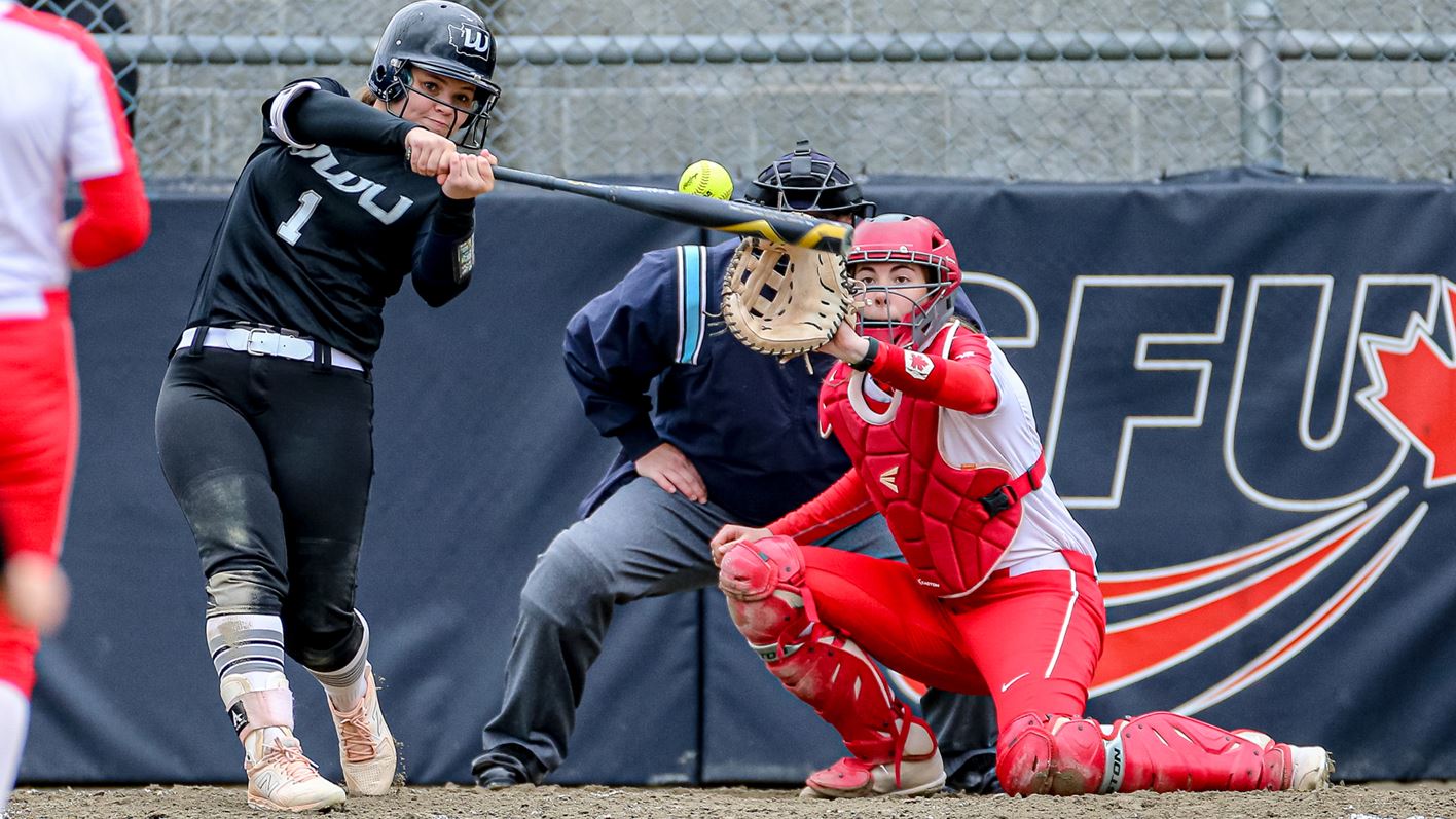 A photo of an opponent swinging on a pitch with an SFU catcher in the background trying to grab the ball.