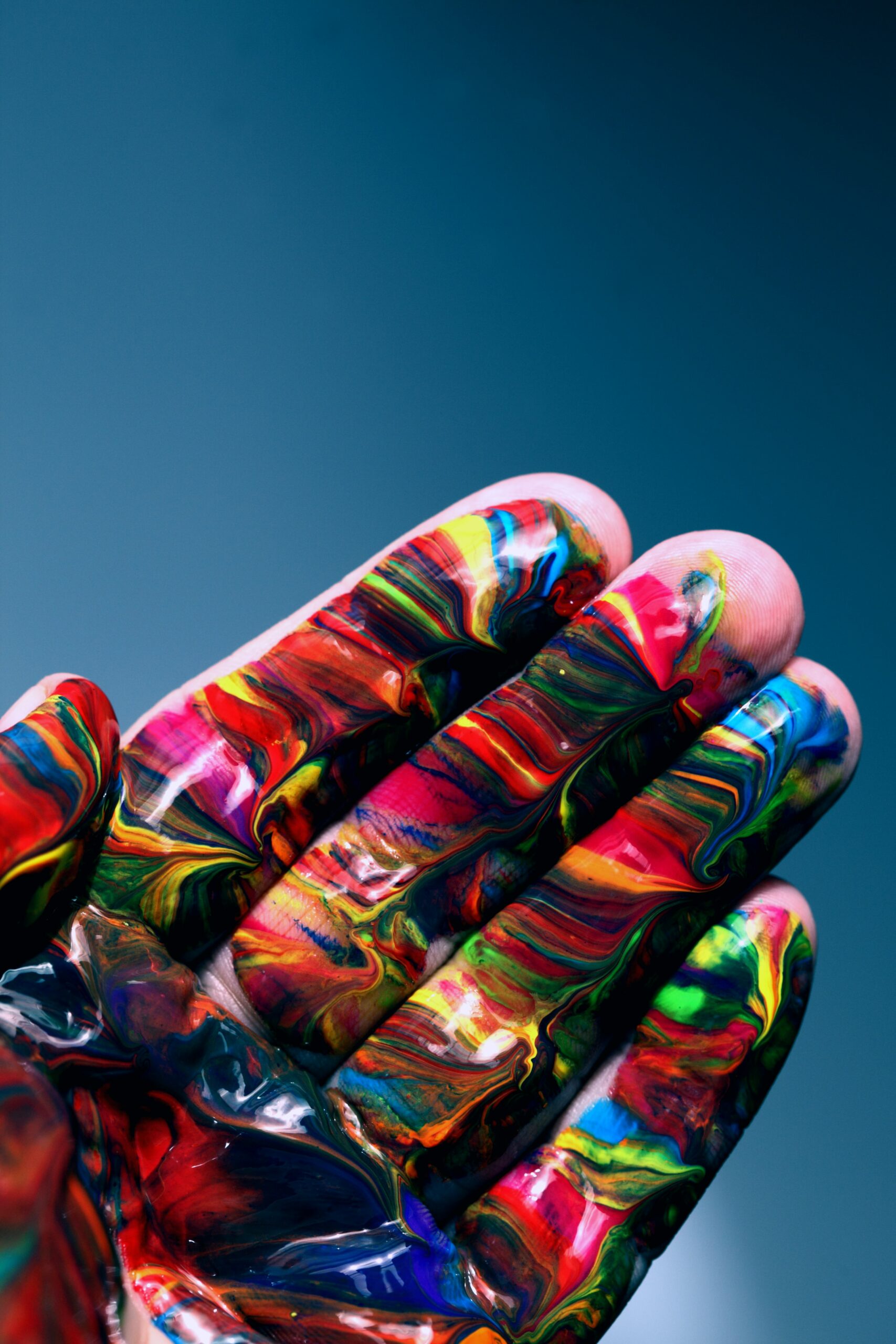 A hand is covered in all colours of paint imaginable. The paint is tightly layered, and looks complex.