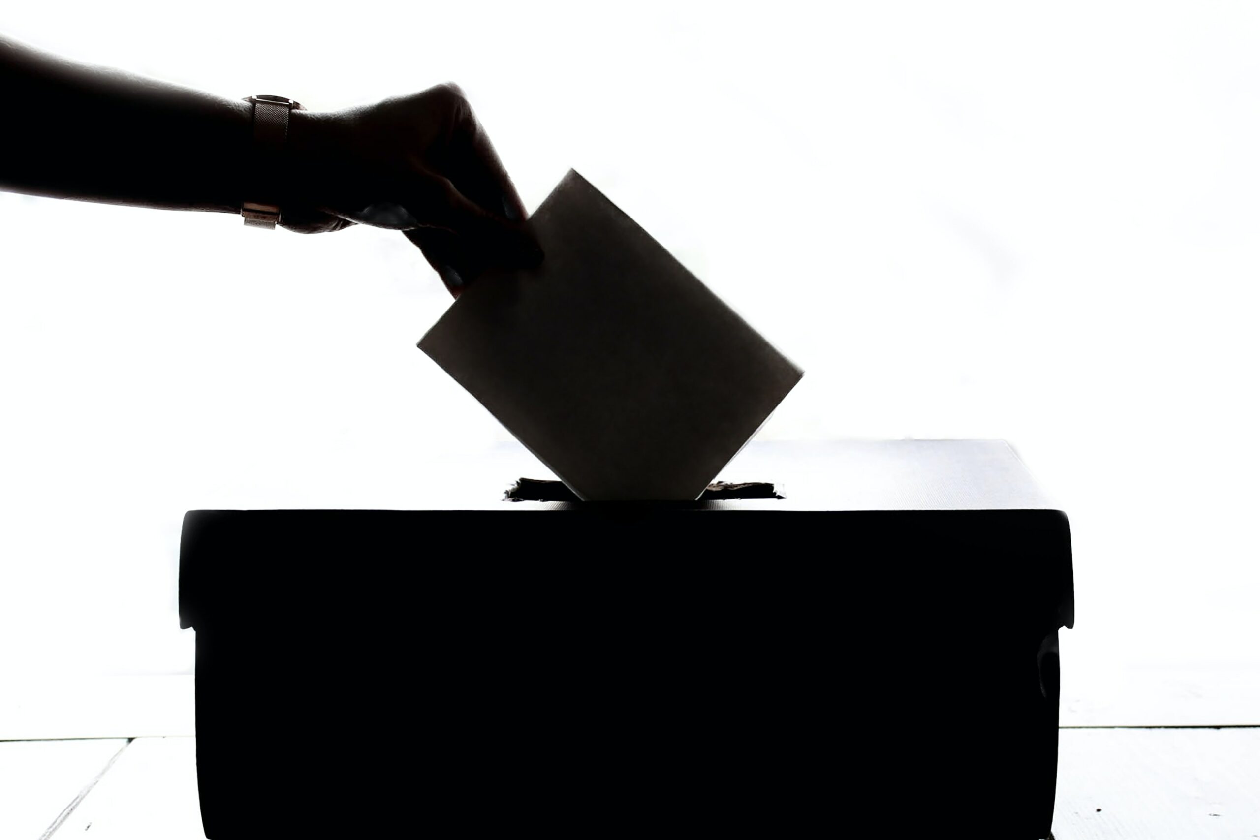 A hand dropping a voter ballot in a box