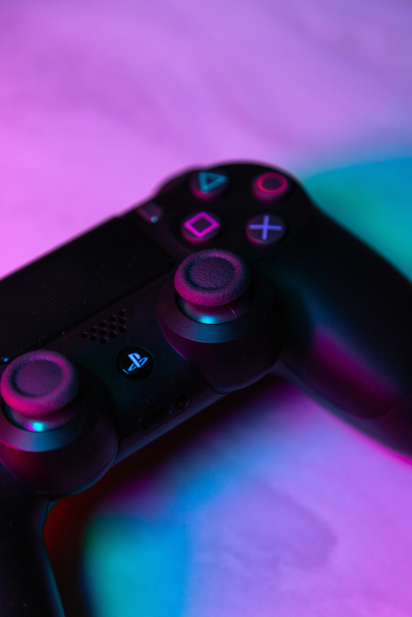 A PlayStation controller lying angled against a purple and turquoise background