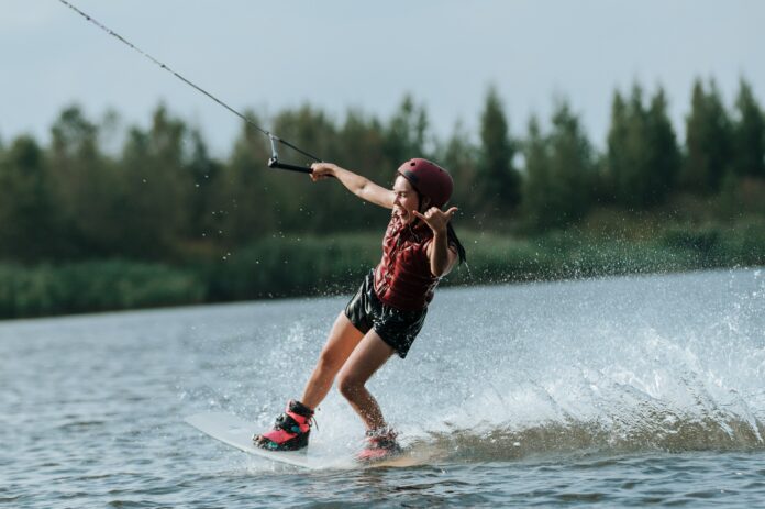 A woman pictured wakeboarding putting up a 'hang loose' sign to the camera.