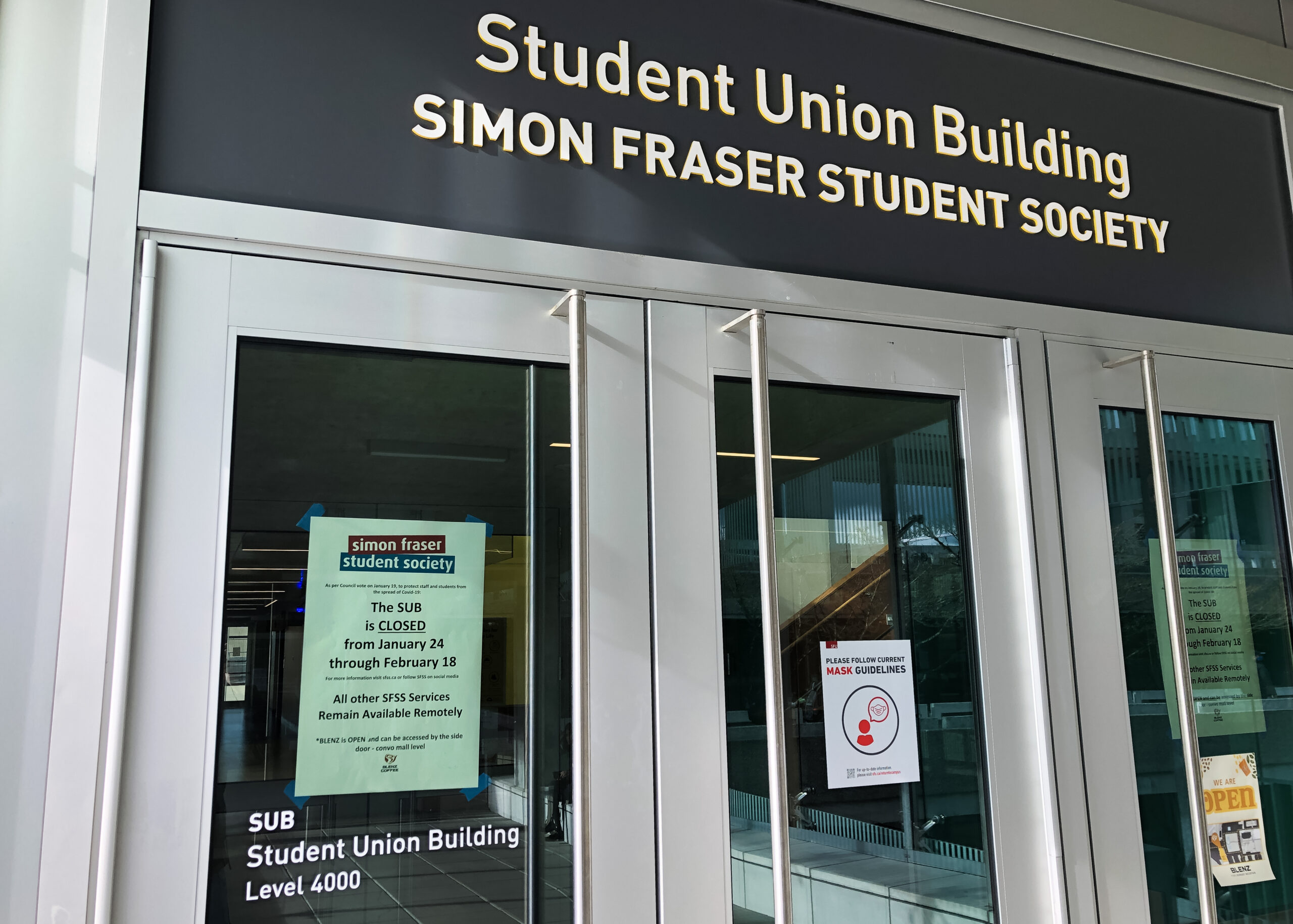 A photo of the Student Union Building. The doors are shown with a note from the SFSS taped to the inside, reading: “The SUB is closed from January 24 through February 18.”