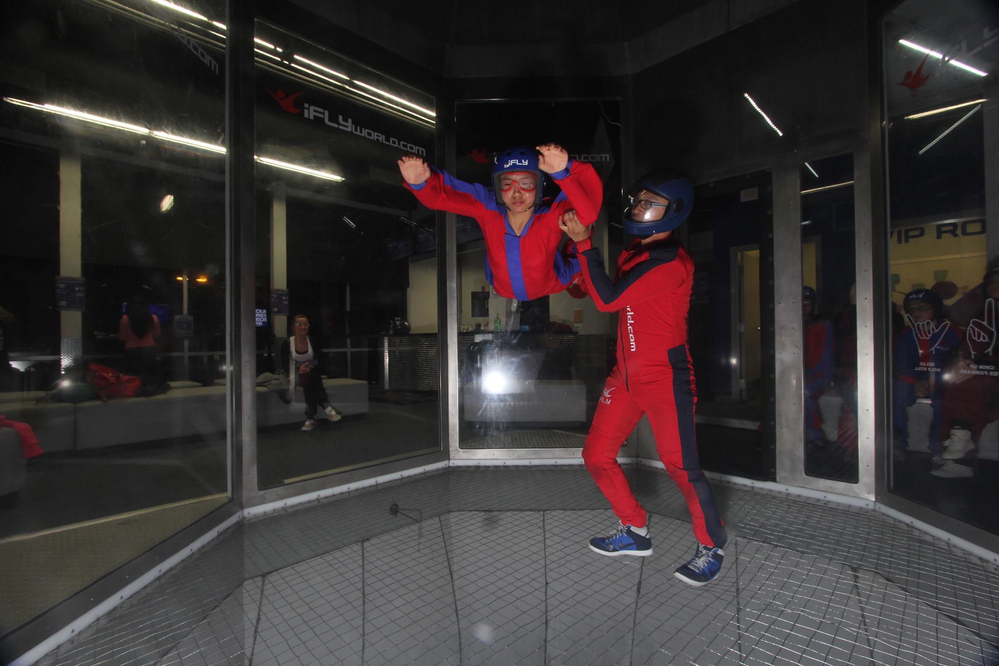 Charlene flying in an indoor wind tunnel with an instructor holding on to her.