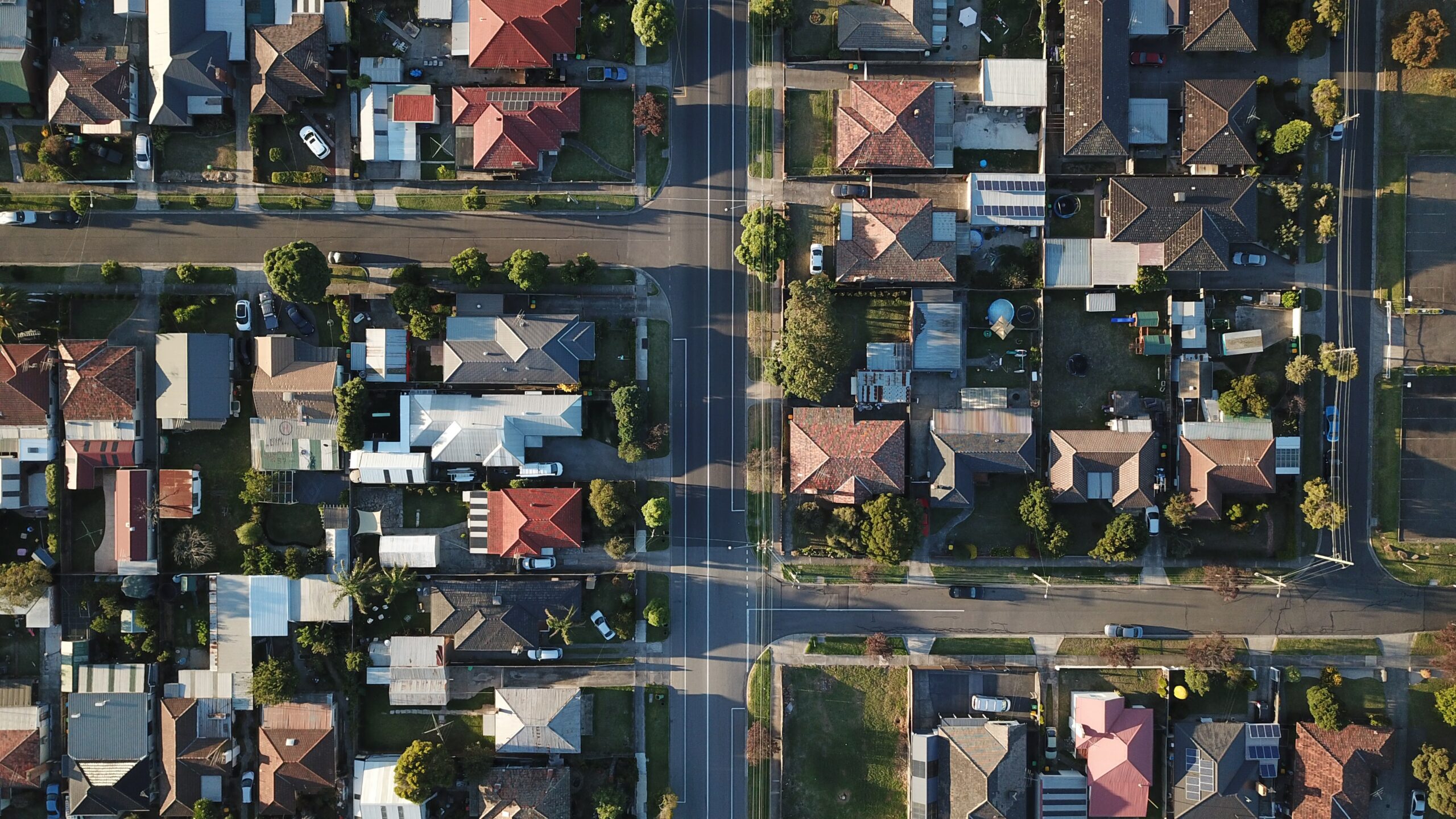 A birds-eye-view of a suburban landscape. Visible are cars, solar panels, rooftops, and roads.