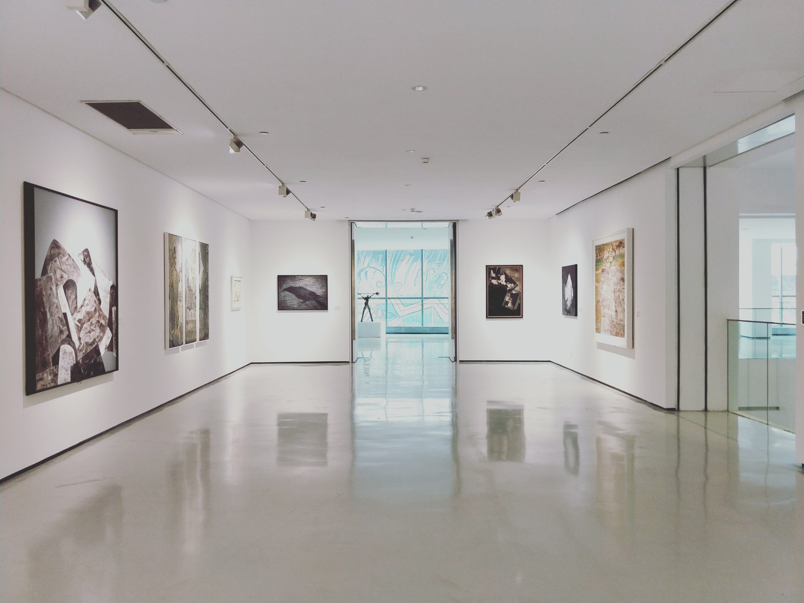An empty gallery with white walls featuring large landscape paintings