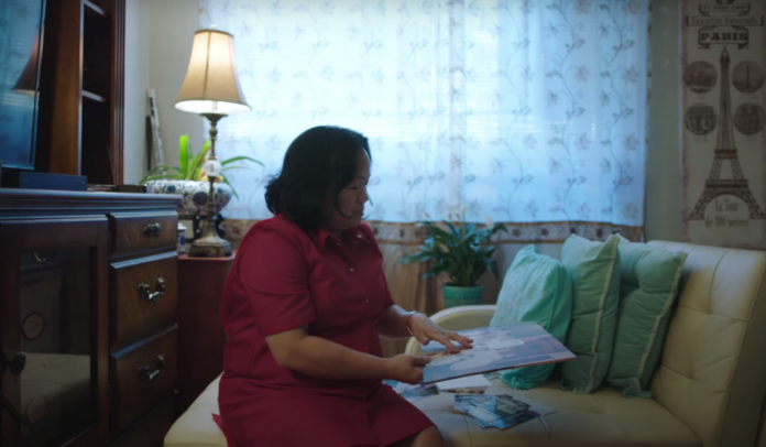 A Filipinx woman, sitting in a living room and studying family photos.