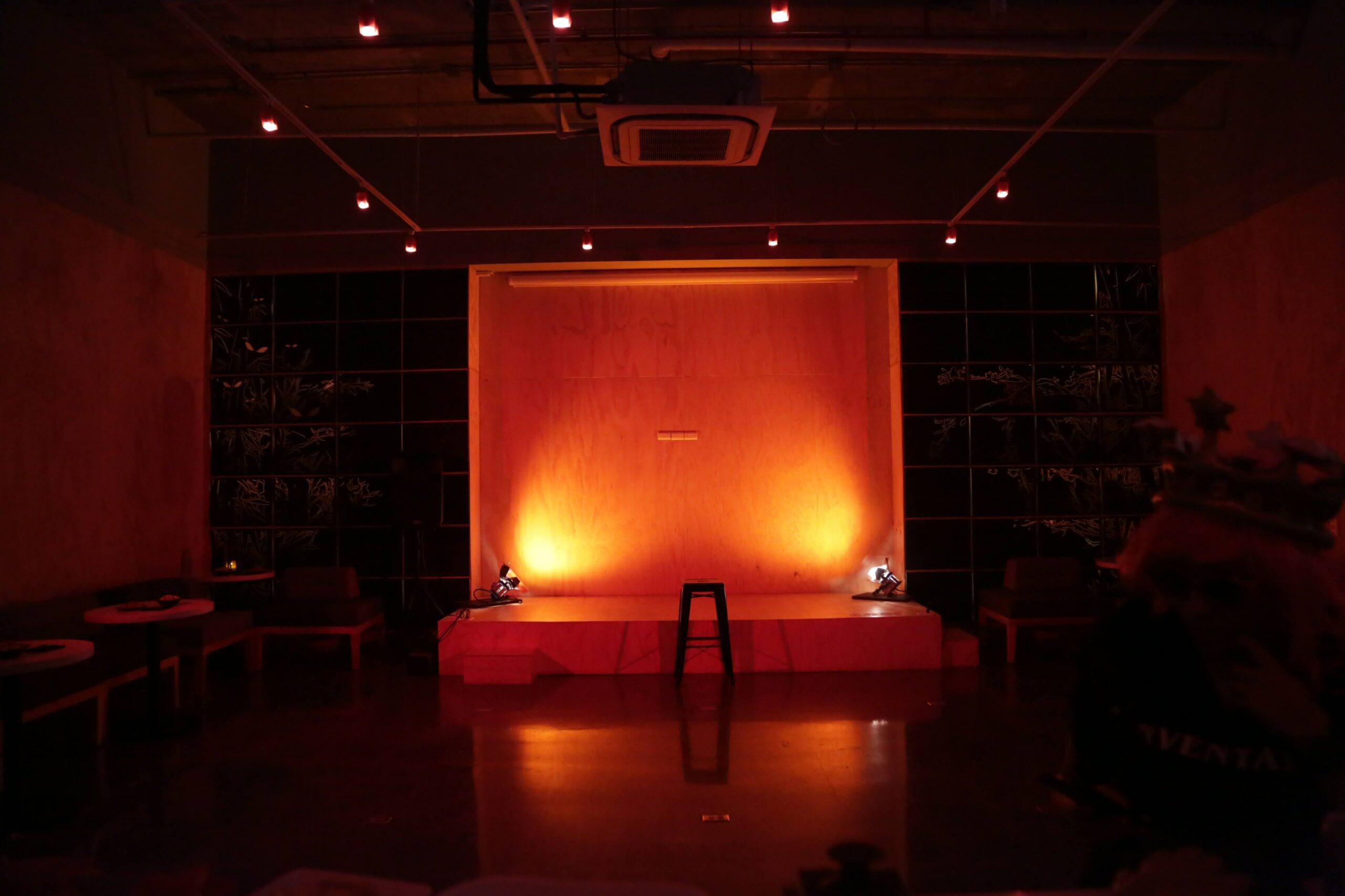 An empty stage in an empty room with orangey-red mood lighting.