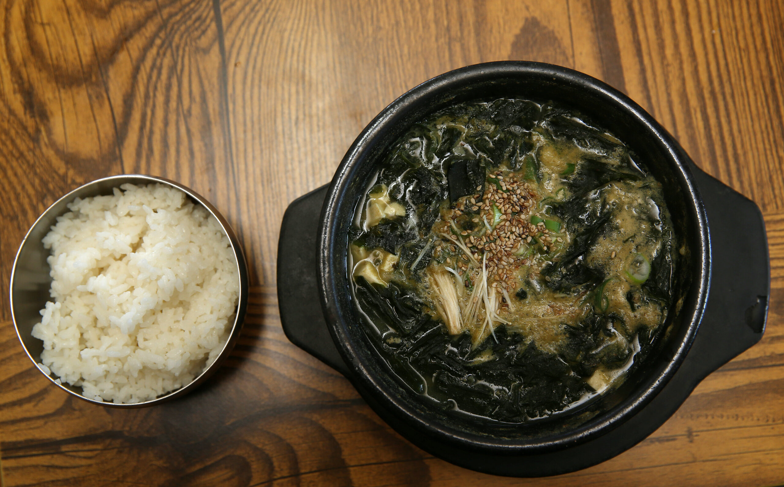 Bowl of seaweed soup served on a brown table with a bowl of rice