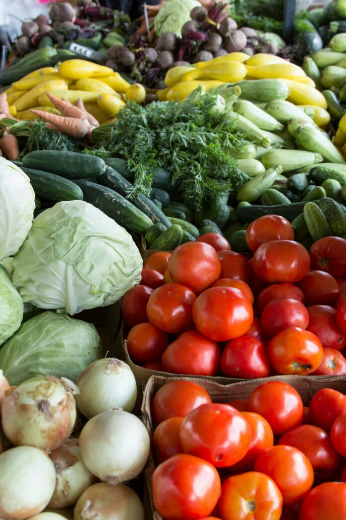 The photo is a close-up picture on multiple piles of fresh vegetables. In the picture are onions, tomatoes, lettuce, carrots, cucumbers, and squash.
