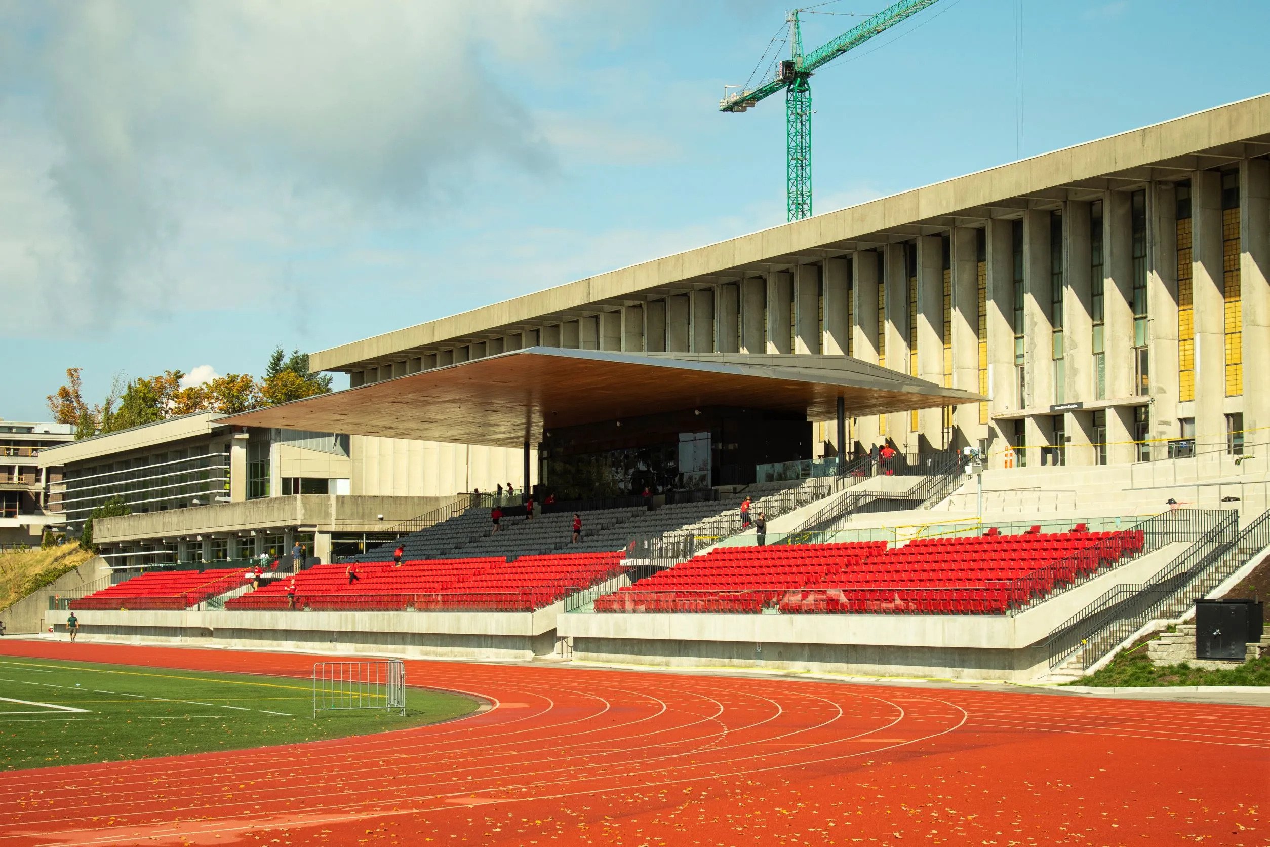 Photo of the SFU stadium. The stands are nearly empty, only a few people walking. The outdoor stadium is seen with a sunny sky behind.