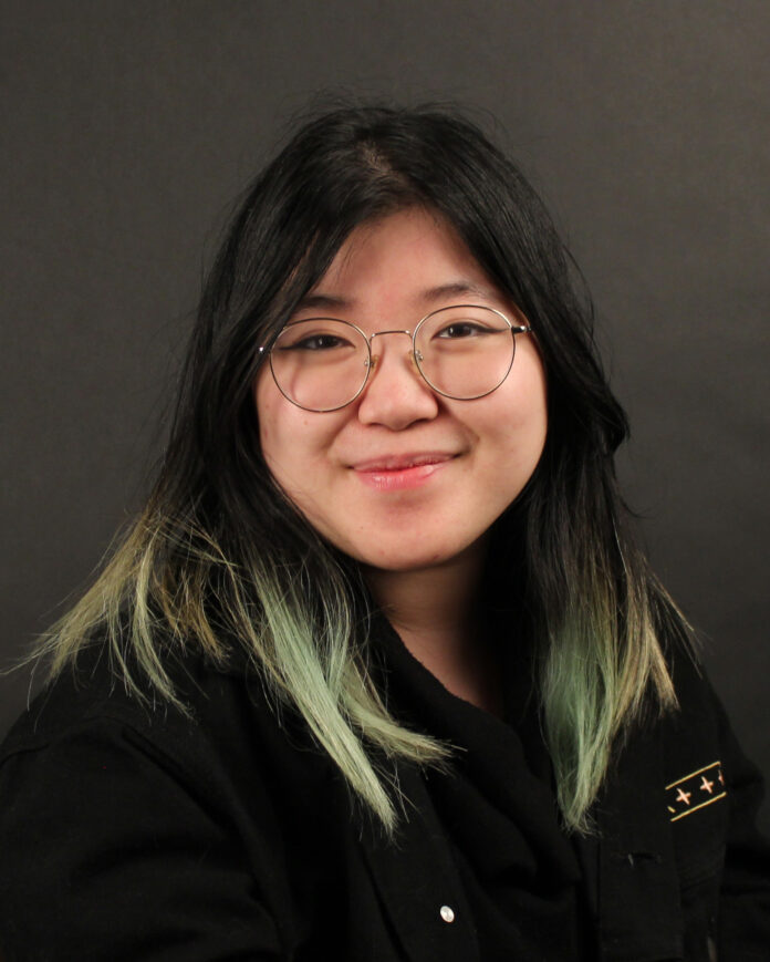 A photo of Humour editor, Kelly Chia, looking very professional and stoic by a wooden bookcase.