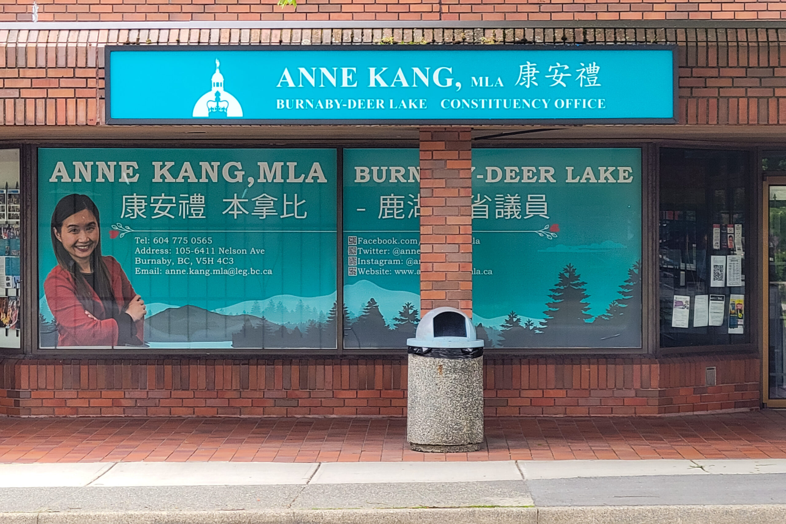 The photo is of the front of NDP MLA Anne Kang's office. The brick building's window has Kang's name and a photo of her face on it.