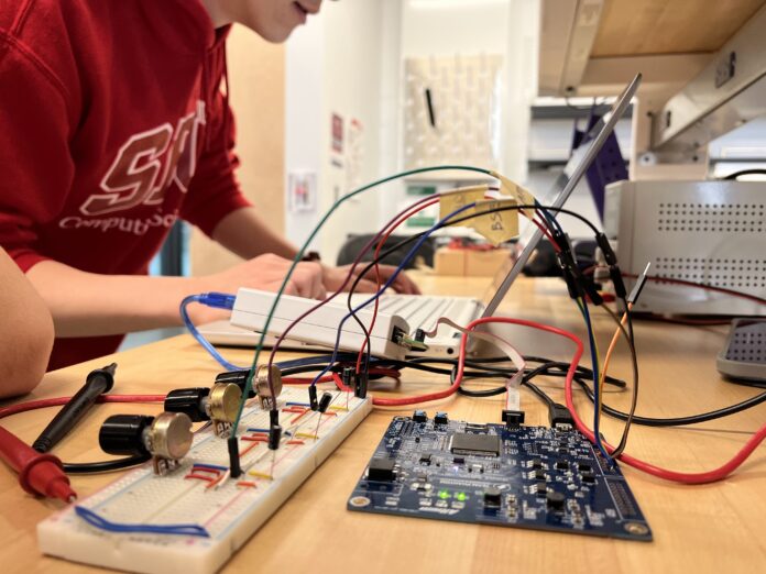 photo of a person working on a laptop with a motherboard in the foreground