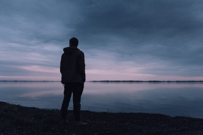 pexels-lukas-rychvalsky-670720 A silhouette of a cis man looking out over a lake.