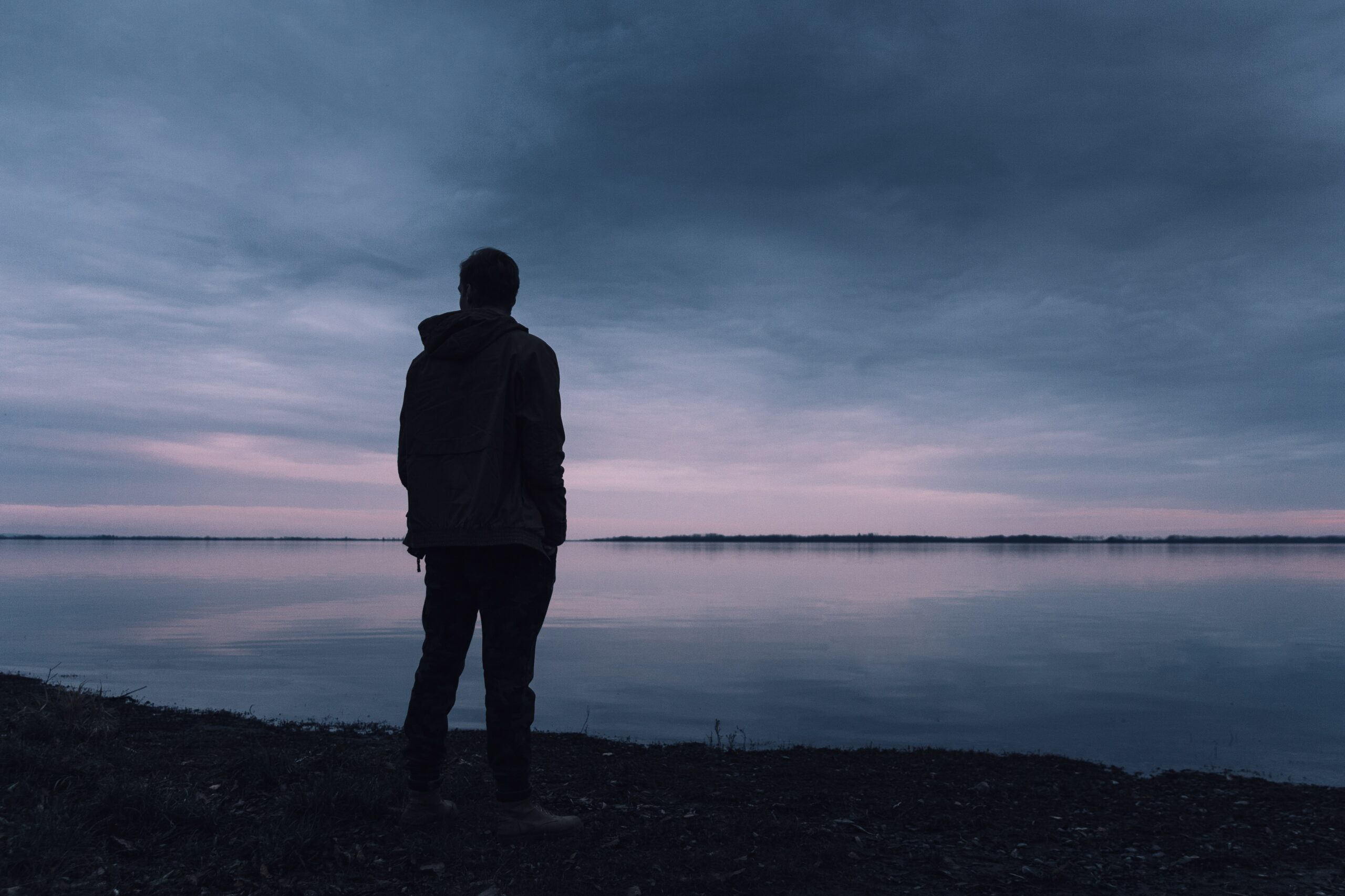A silhouette of a cis man looking out over a lake.