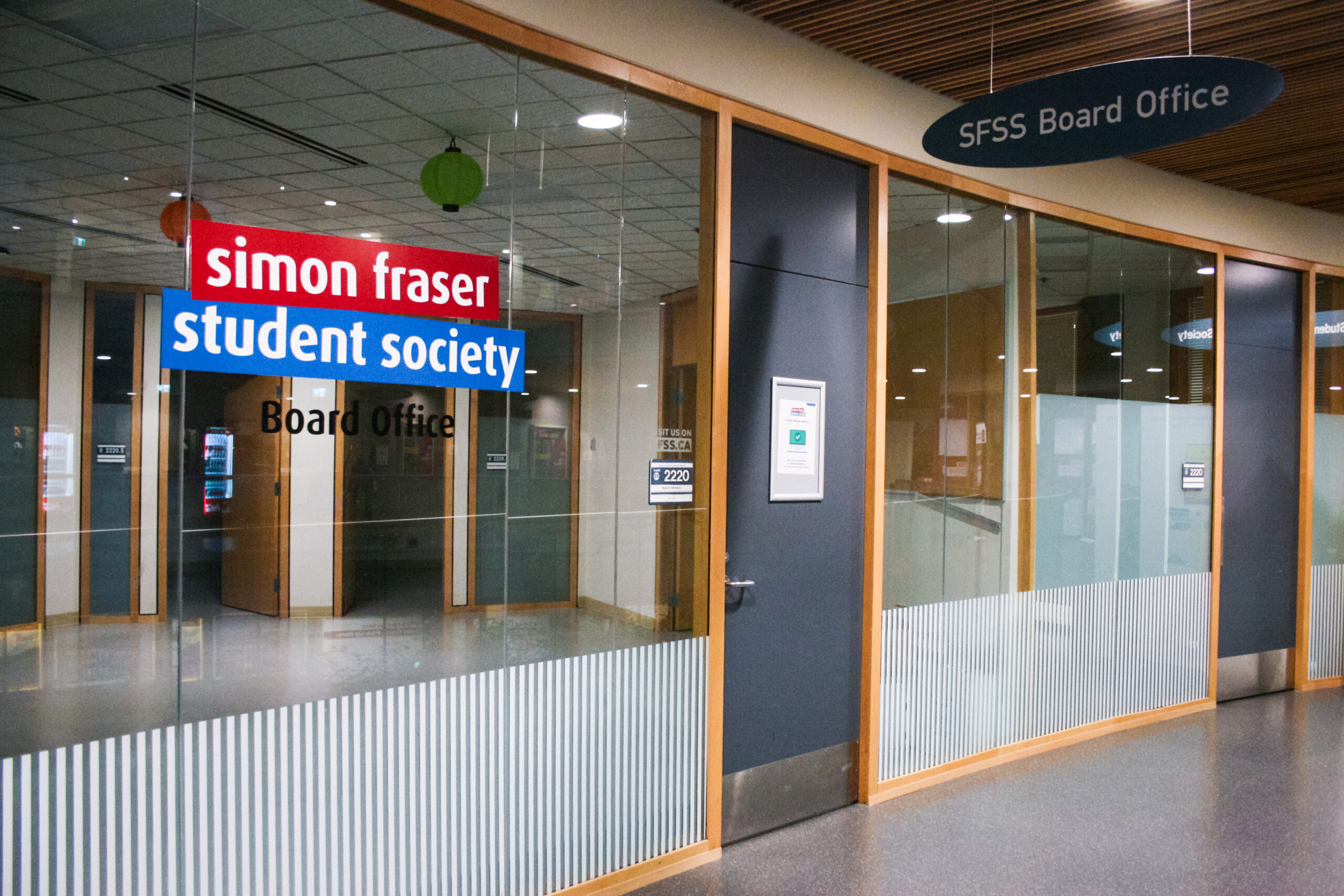 The photo is of the outside of the Simon Fraser Student Society's office. The office has large windows that have their logo printed out.